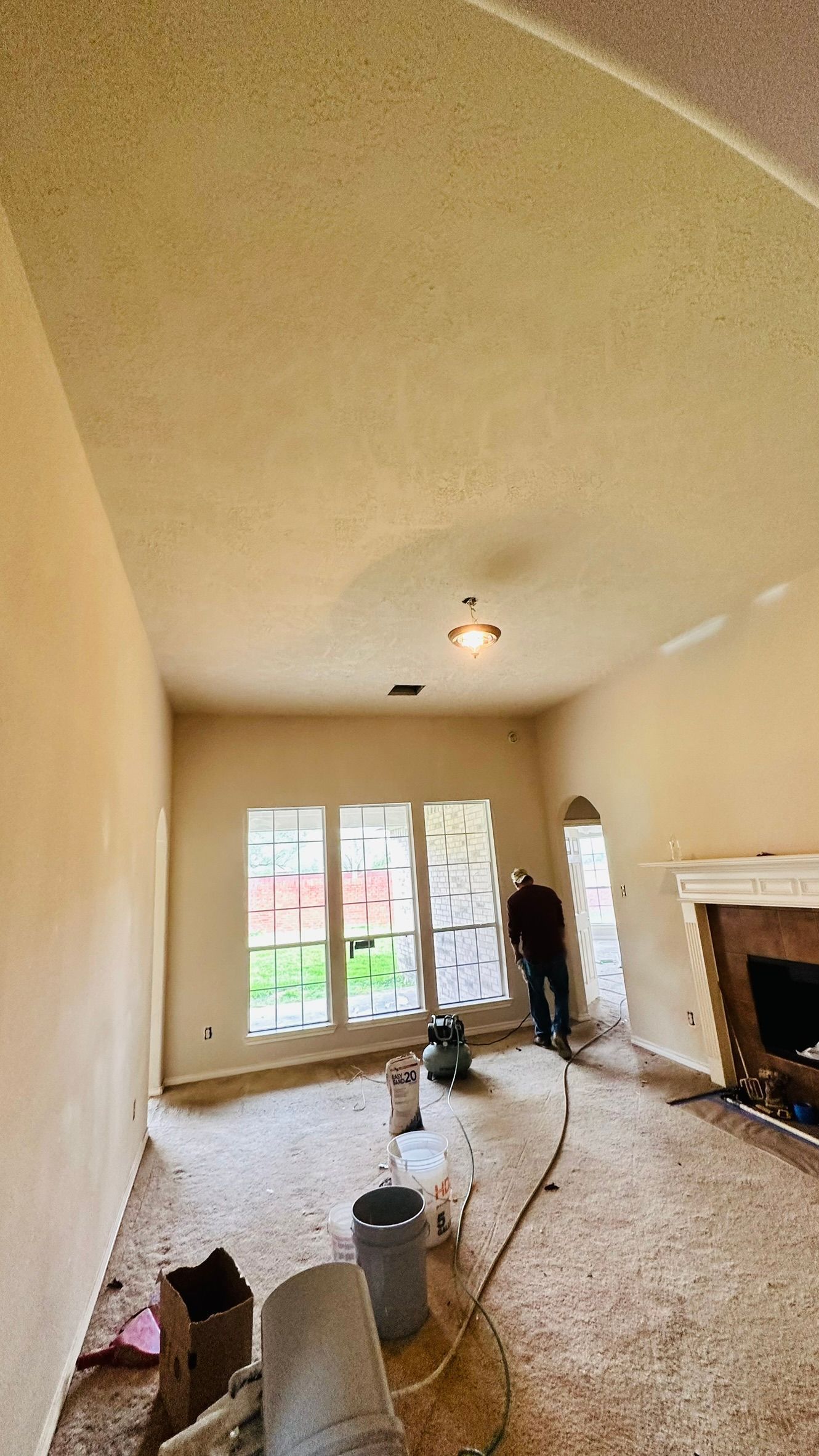Man in room using equipment on wall, room under renovation with bare floors, windows, and fireplace.