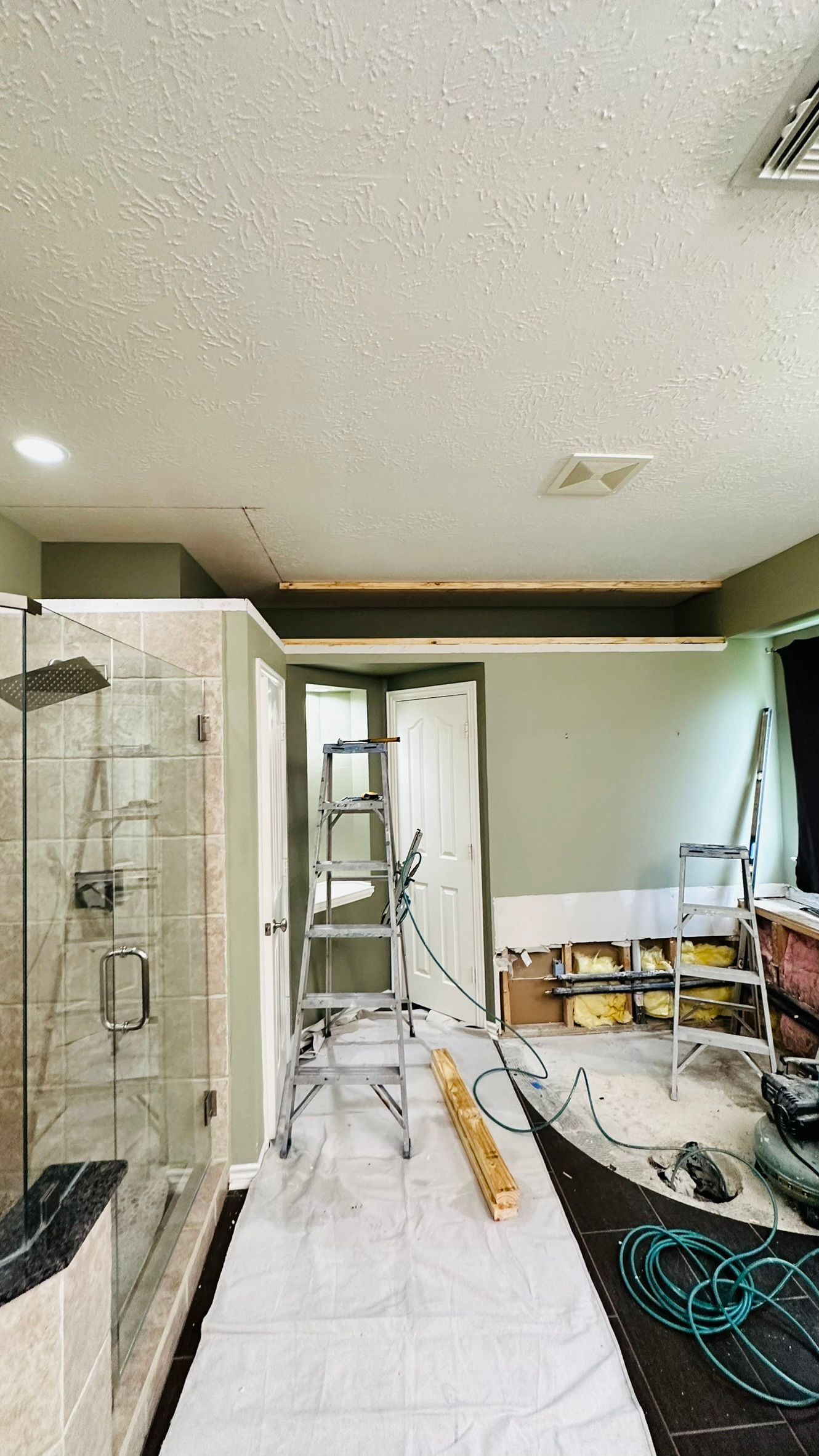 Renovation room with drywall, a ladder, tools, and a tiled wall under construction
