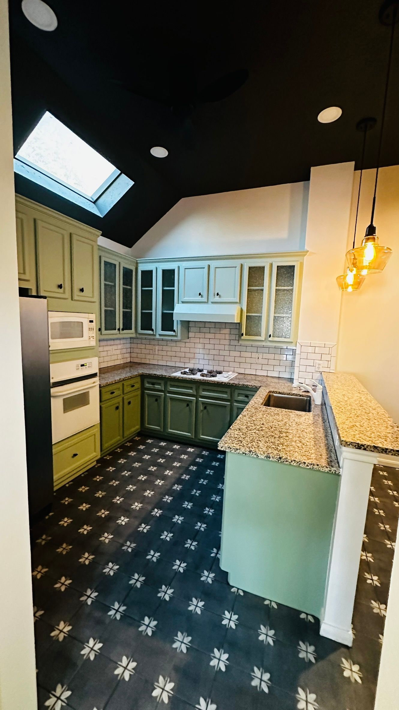 Bright kitchen with green cabinets, black ceiling, skylight, and patterned floor tiles.
