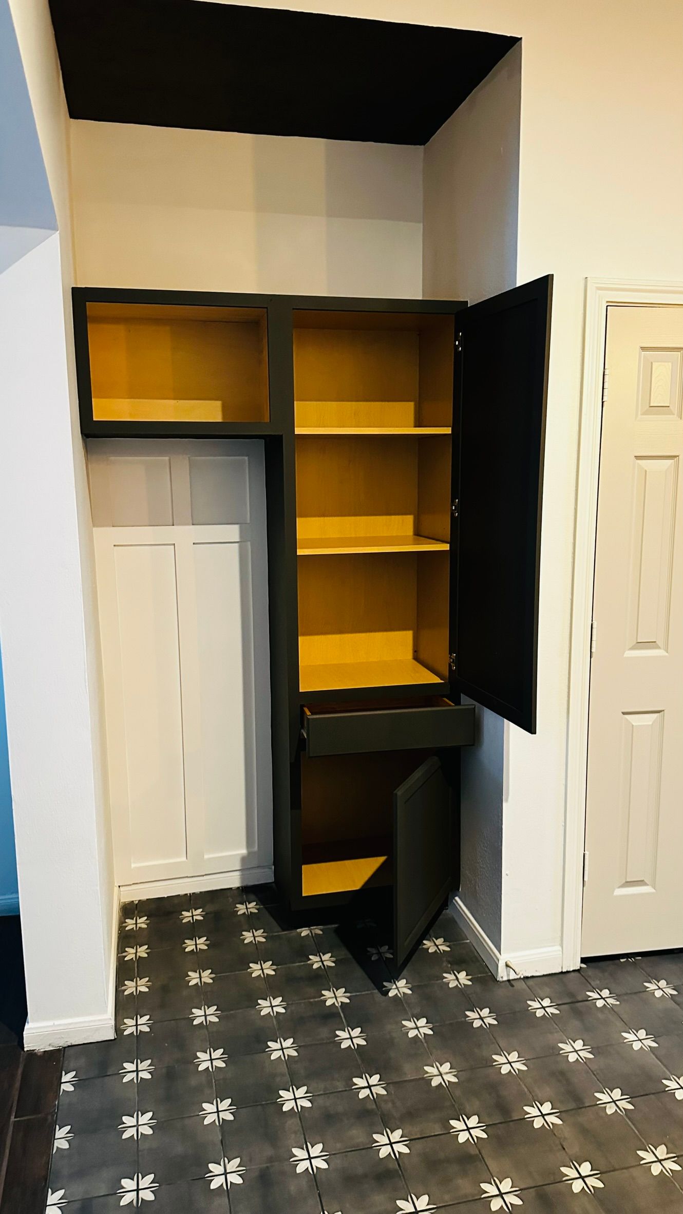 Open closet with black cabinet doors, yellow shelves, and a white door beneath an overhead cubby.