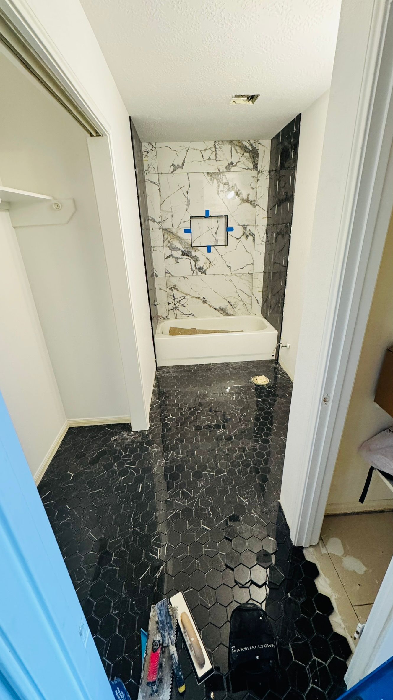 Narrow hallway with black flooring leading to a small bathroom under renovation, with exposed wall and tiles at the end