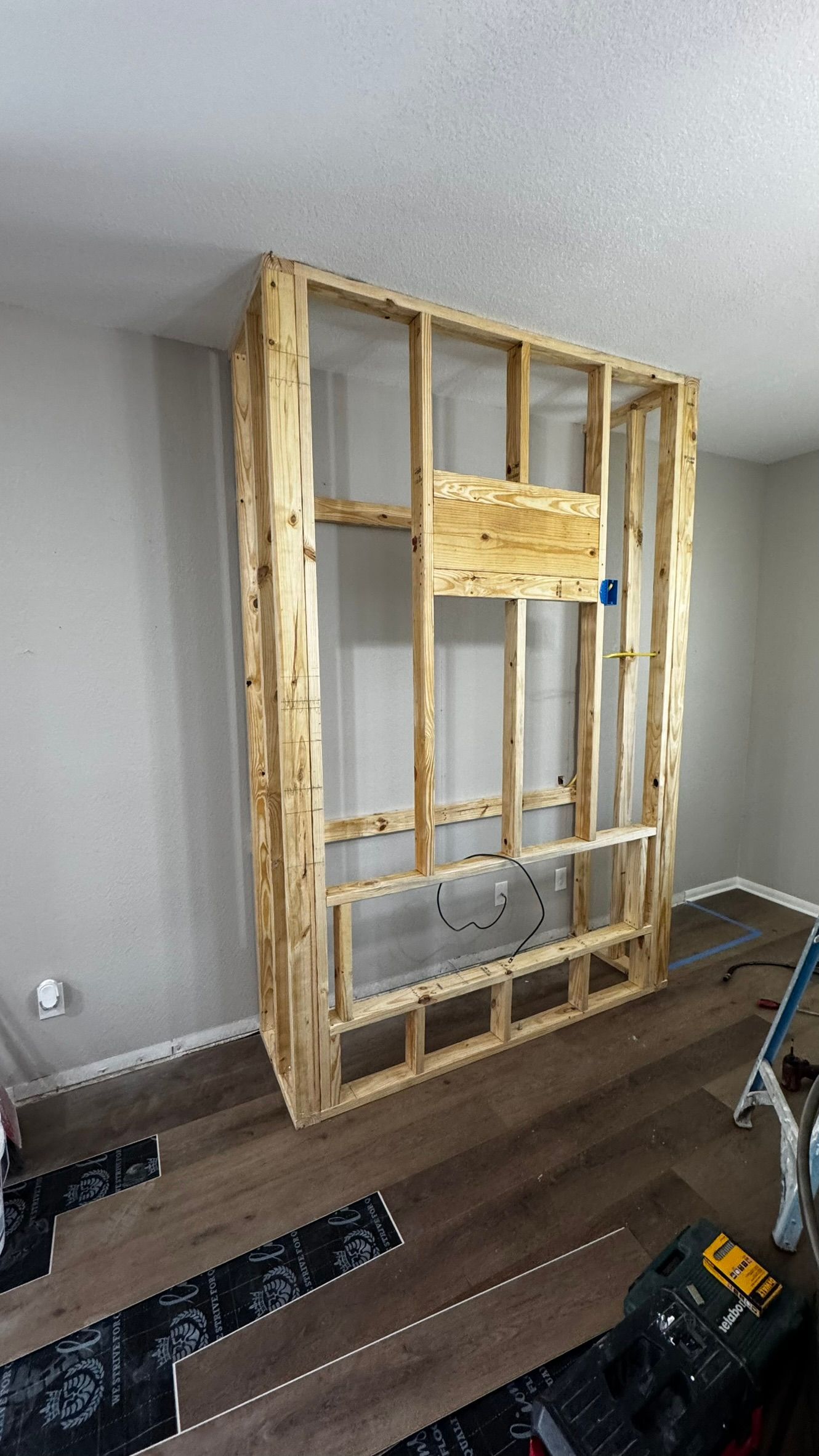 Exposed wood framing against a white wall in a room, with tools and flooring materials nearby.