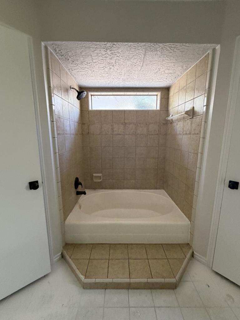 Tiled bathroom alcove with a built-in bathtub and small frosted window above it.