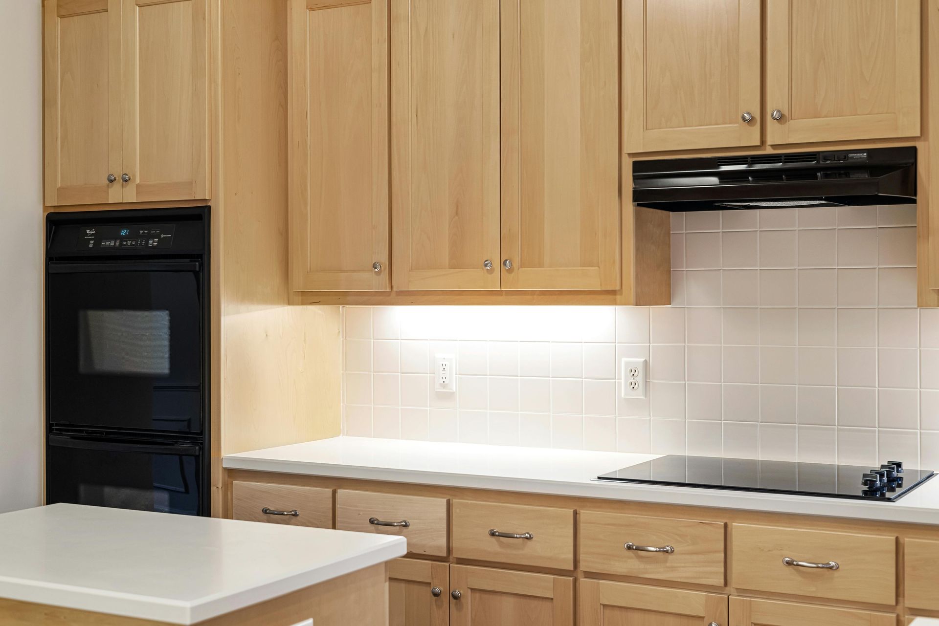 Kitchen with light wood cabinets, white countertops, and black oven and stovetop.