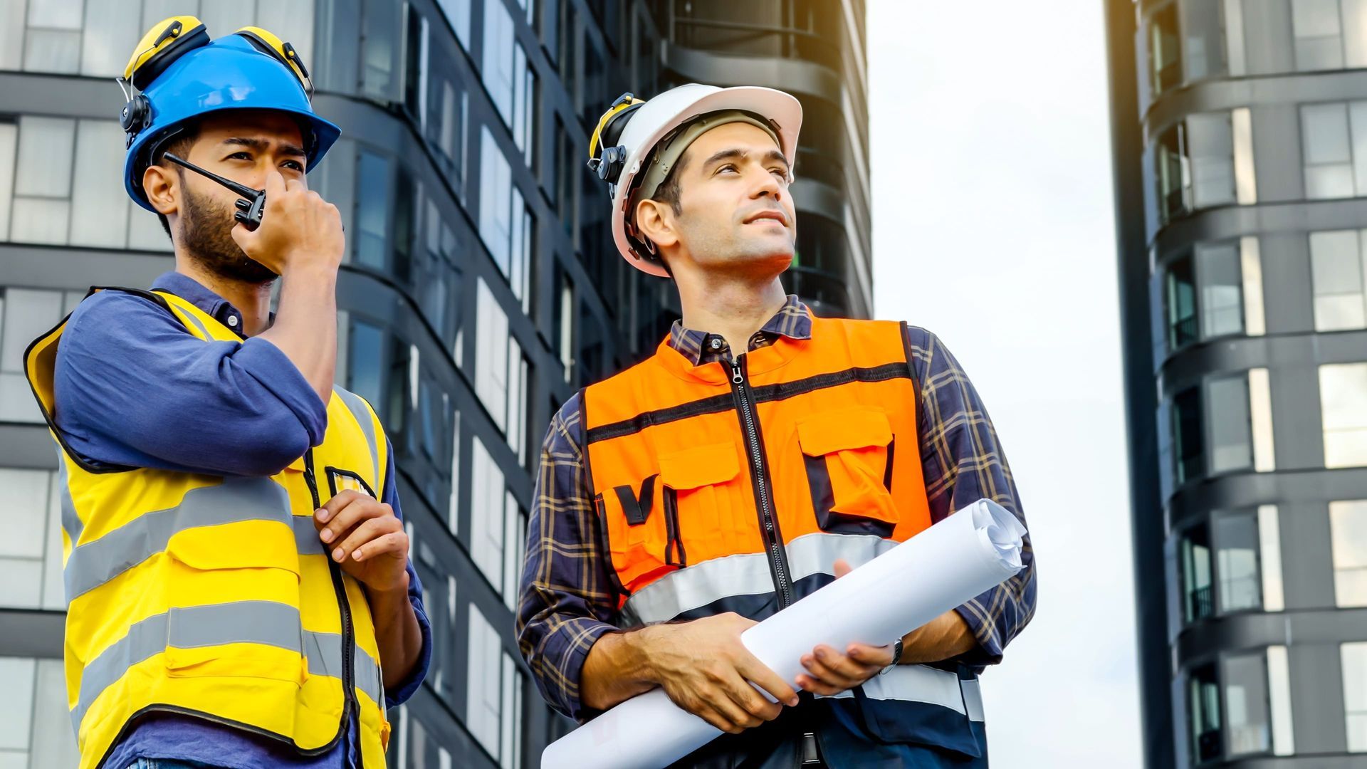 Two construction workers are standing next to each other in front of a building.