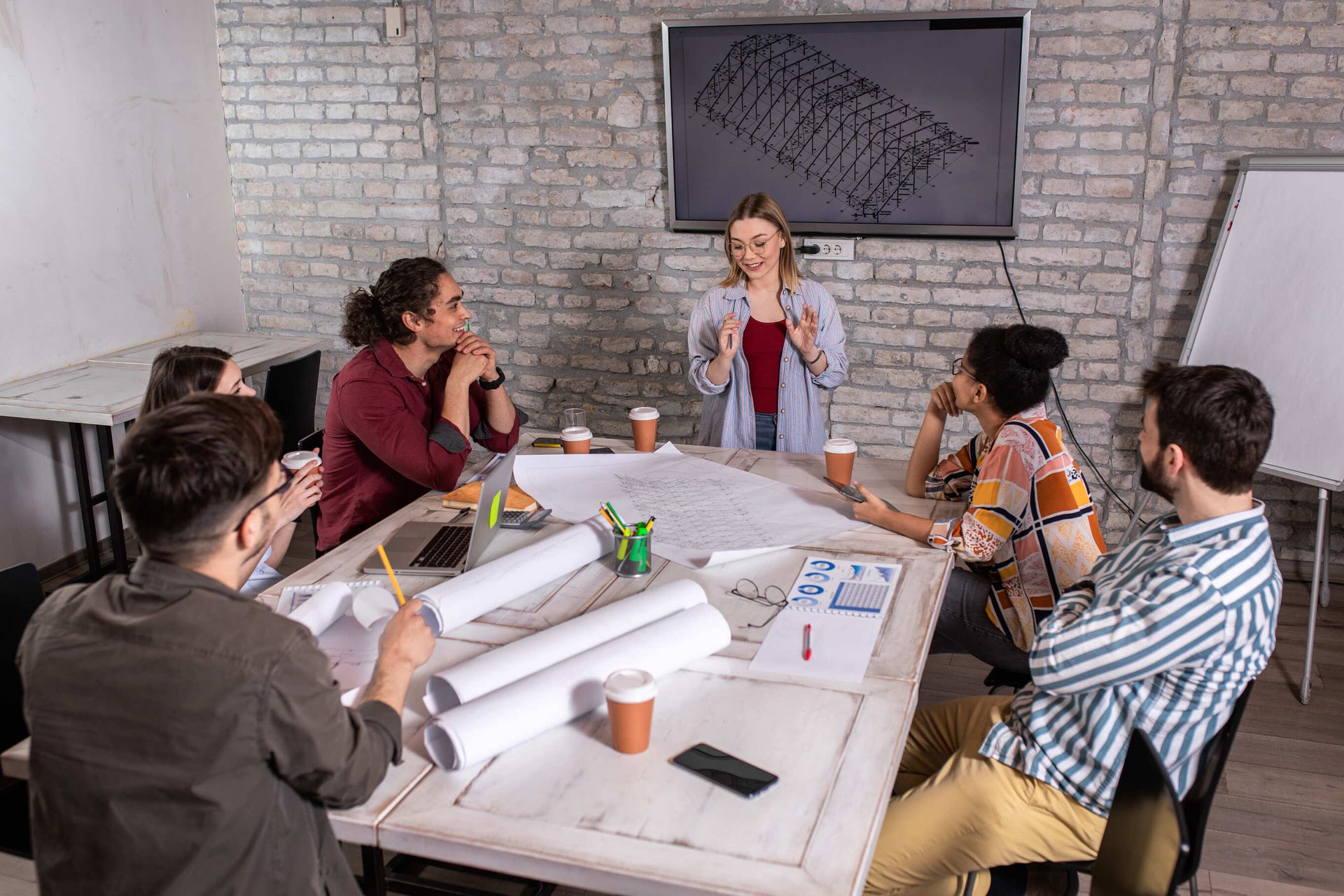 A woman is giving a presentation to a group of people sitting around a table.
