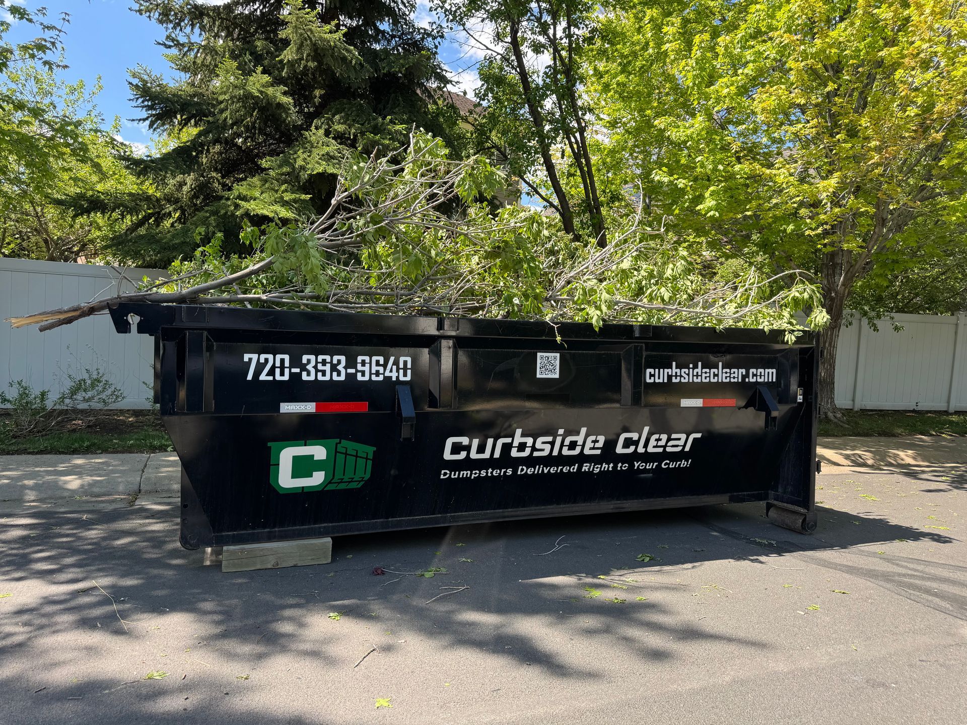 Black Curbside Clear dumpster parked by trees on a sunlit street