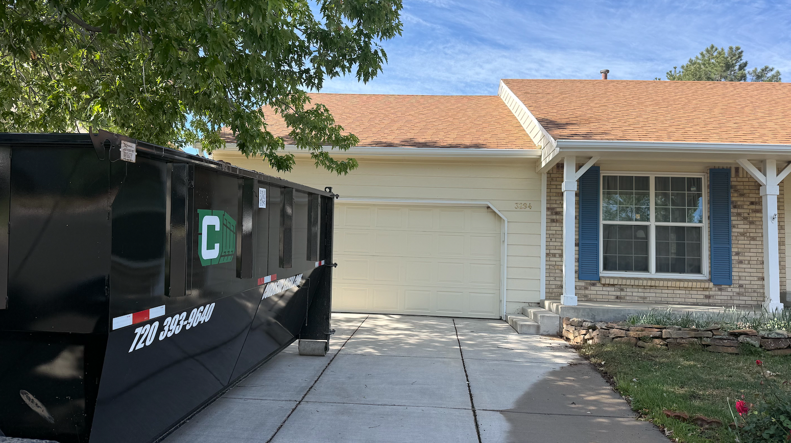 Driveway with a black dumpster beside a beige garage and house front.