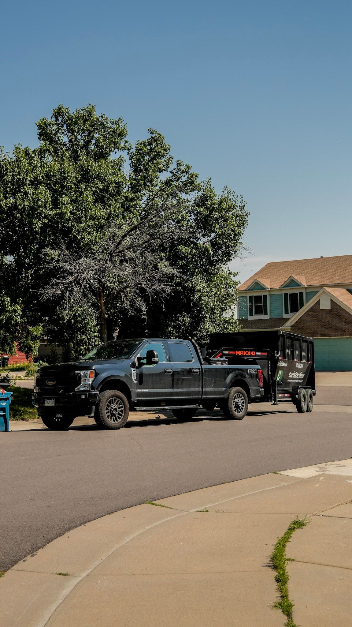 Black pickup truck parked on a suburban street beside a tree and a house under a clear blue sky