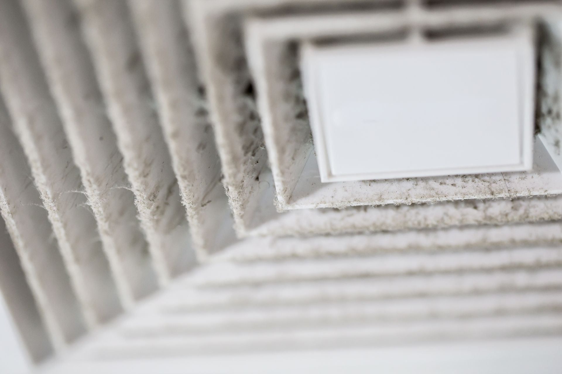 Close-up of a dusty white ceiling air vent with heavy dust buildup on the louvers