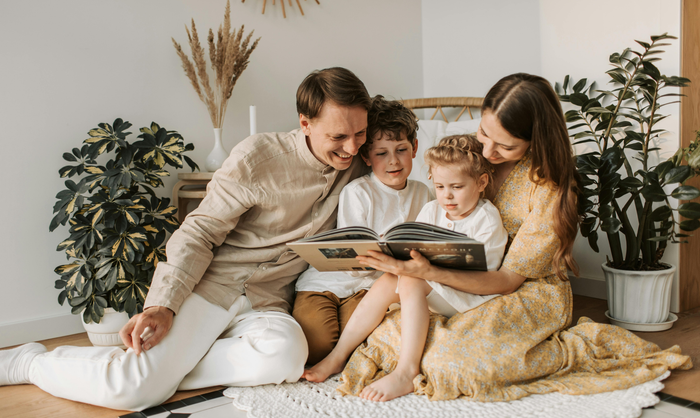 A family sitting on the floor in a bright room, smiling while looking at a book together. A family sitting on the floor in a bright room, smiling while looking at a book together.