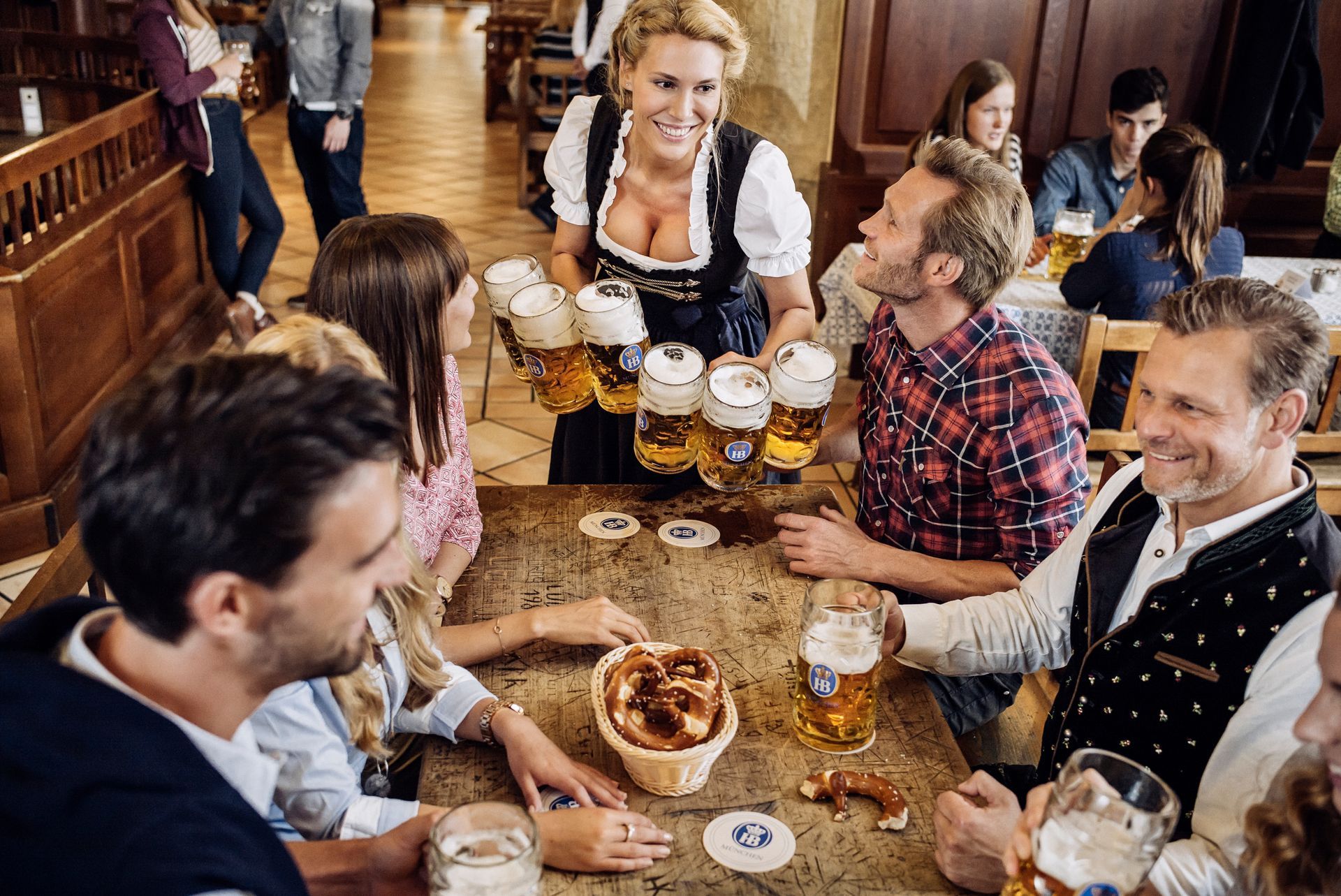 Friends clinking beer mugs around a pub table with pretzels and appetizers, smiling and chatting