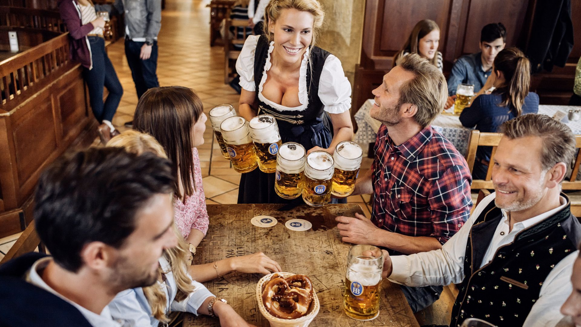 Friends clink beer mugs around a wooden table in a lively pub, with one server smiling at the center.