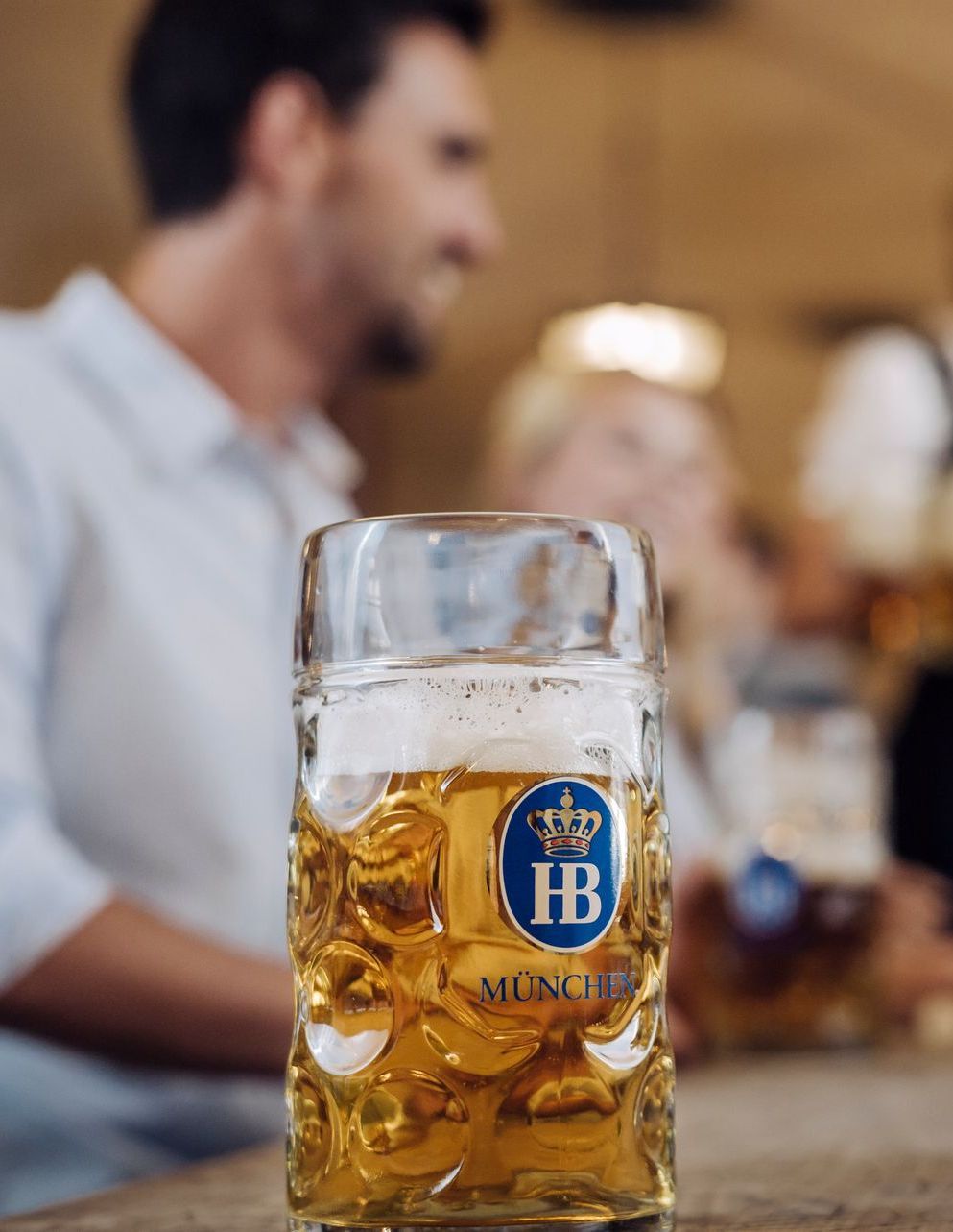 Beer mug with ice and gold Hennessy-style logo on a table in a blurred bar setting
