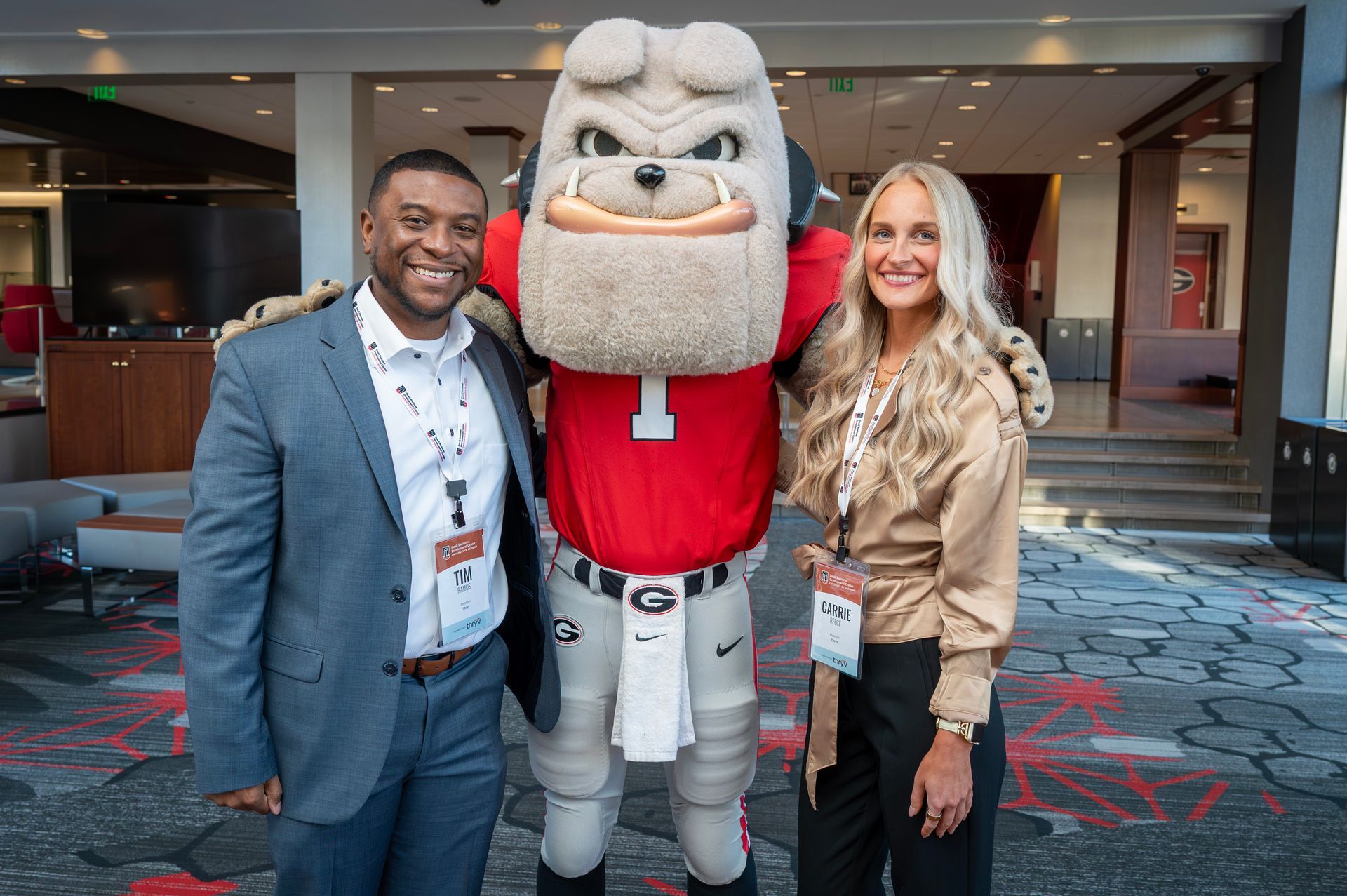 A person in a suit and a person in a beige top pose for a photo with the University of Georgia bulldog mascot.