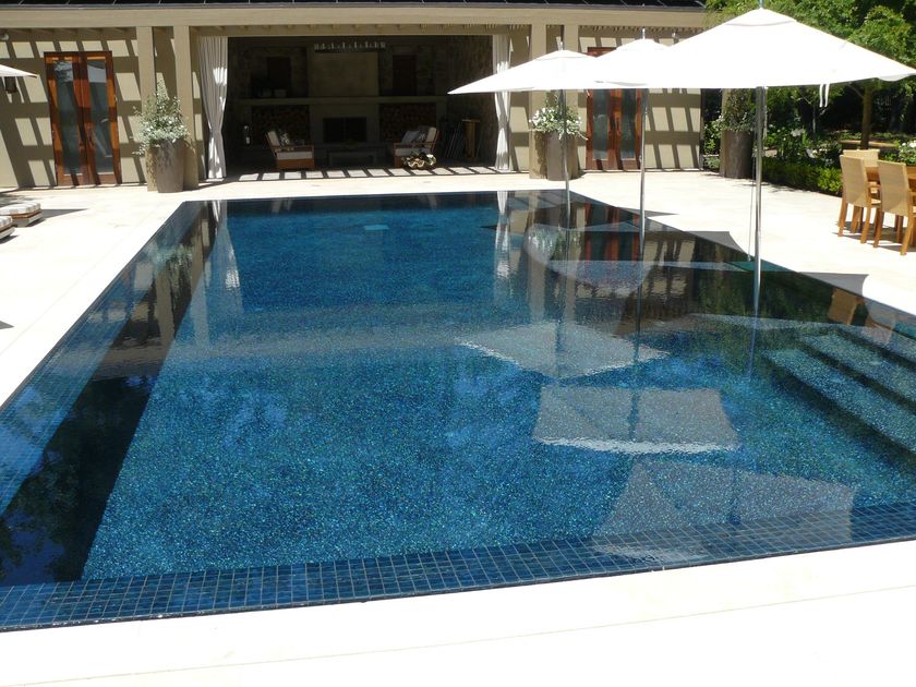 Outdoor swimming pool with blue water, white umbrellas, and patio chairs by a resort building