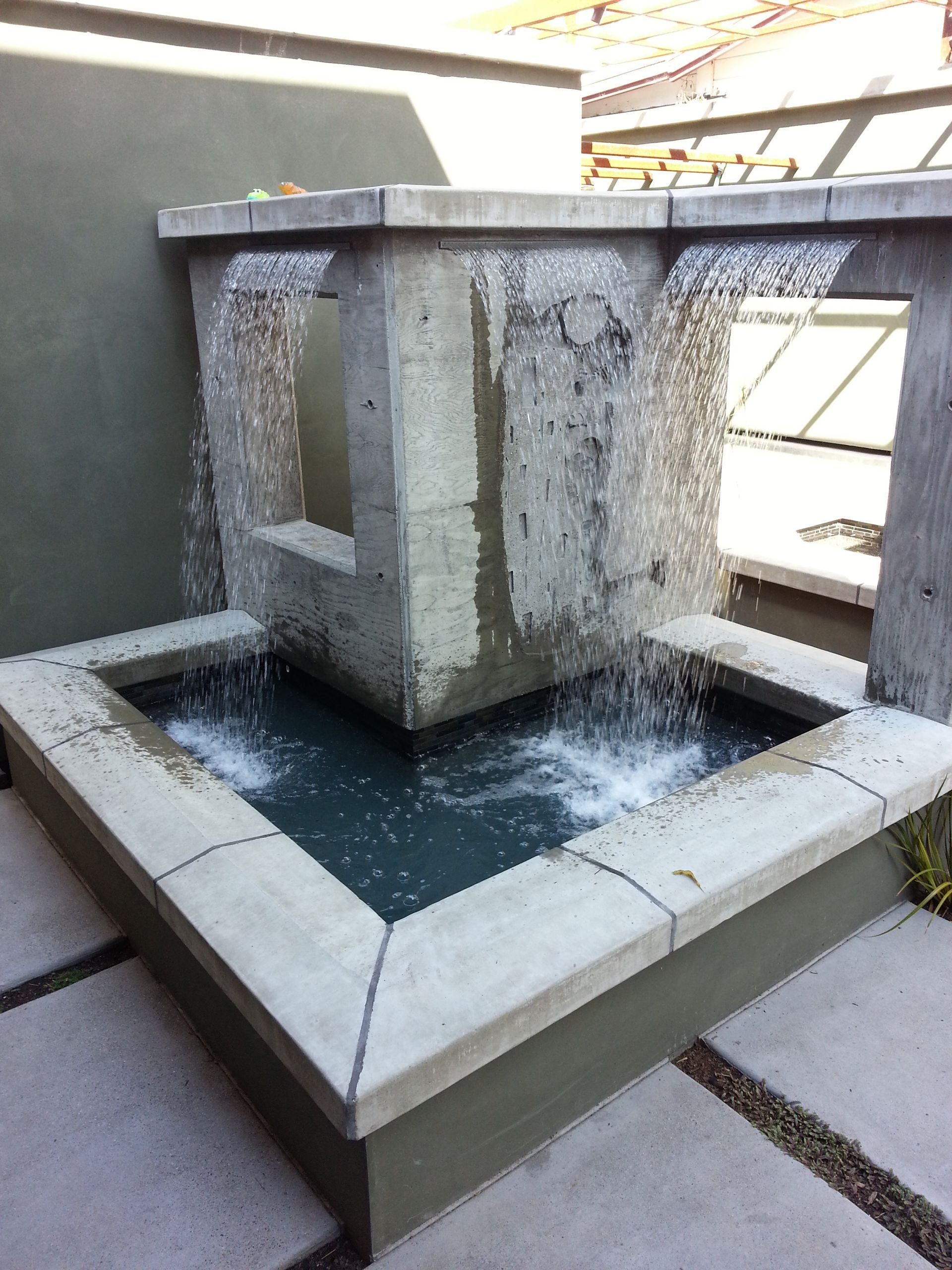 Stone courtyard fountain with water spilling into a square basin in bright sunlight