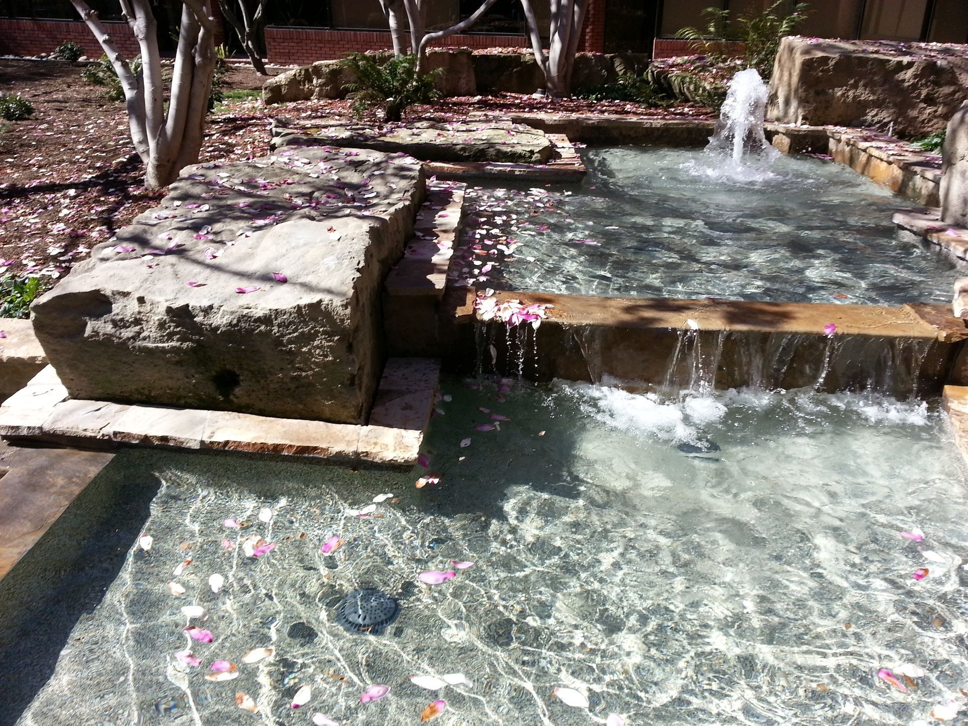 Pool fountain spouting water into a turquoise swimming pool with tiled edge