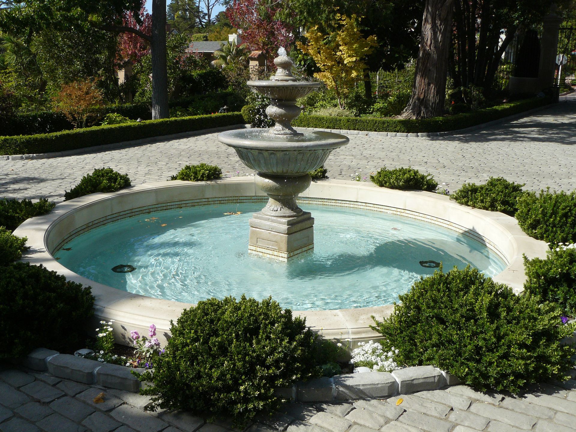 Stone fountain in a landscaped garden with a pale blue basin and trimmed shrubs