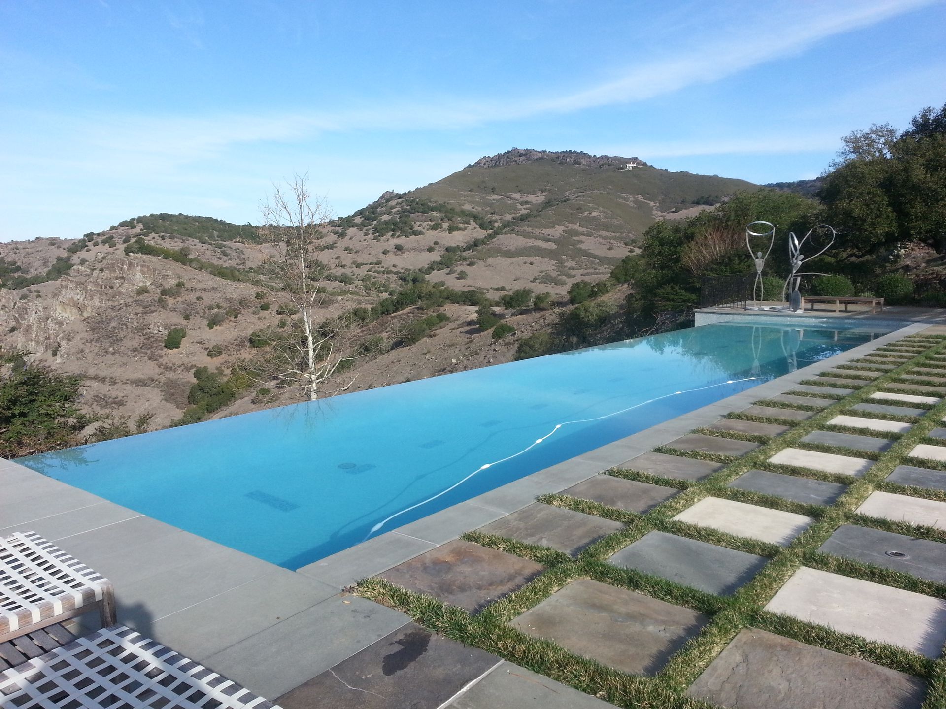 Infinity pool overlooking rocky mountains under a blue sky with stone pavers in the foreground