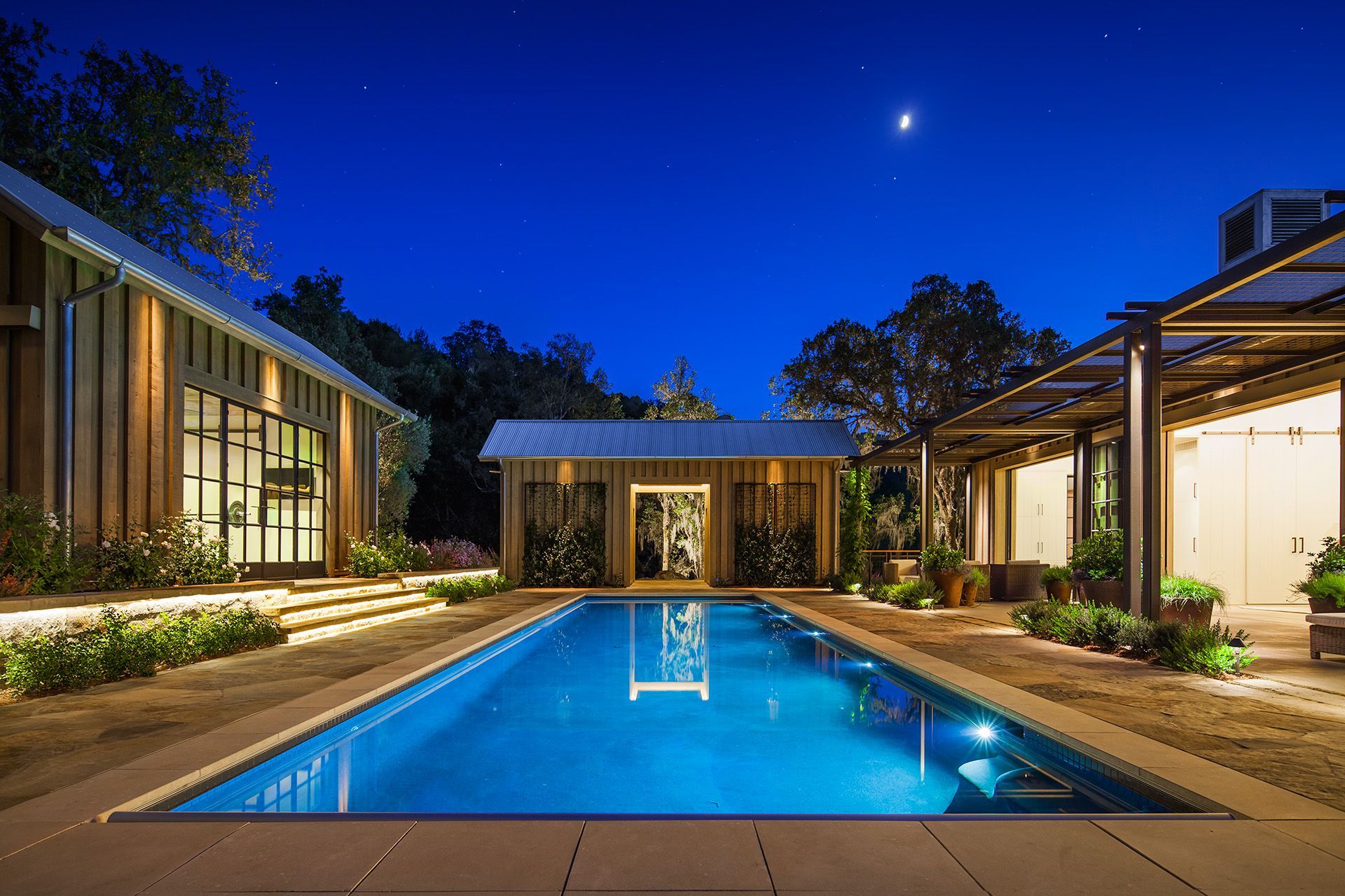 Modern house courtyard with a lit swimming pool at dusk under a deep blue sky