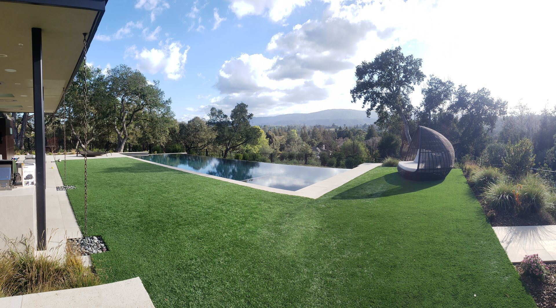 Modern backyard with an infinity pool, green lawn, and mountains in the distance