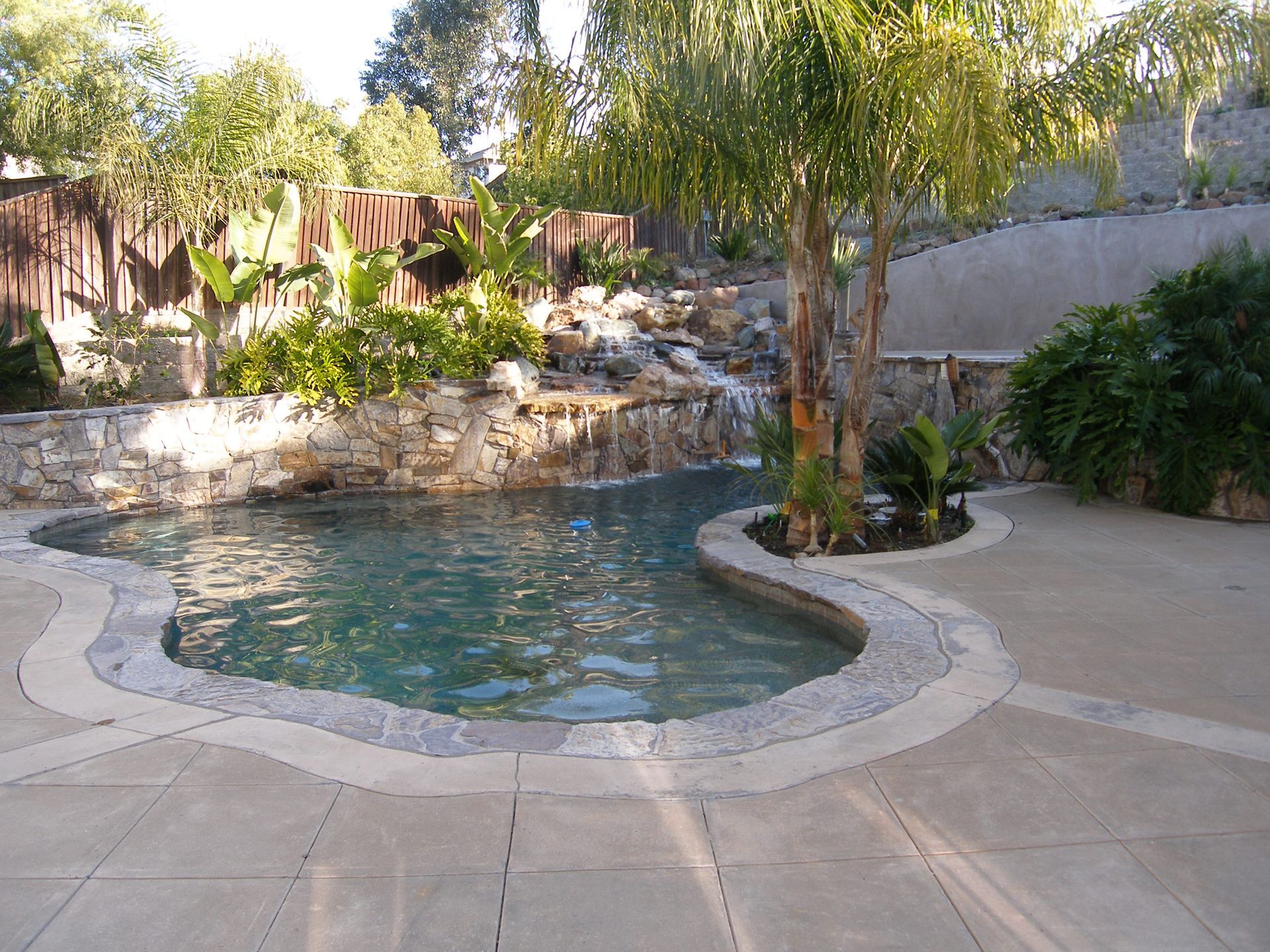 Backyard pool with a natural rock waterfall, curved patio, and tropical landscaping