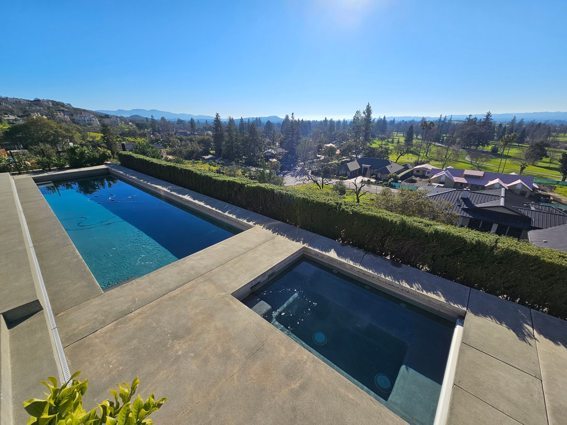 Modern backyard with an infinity pool, hot tub, and scenic hillside view