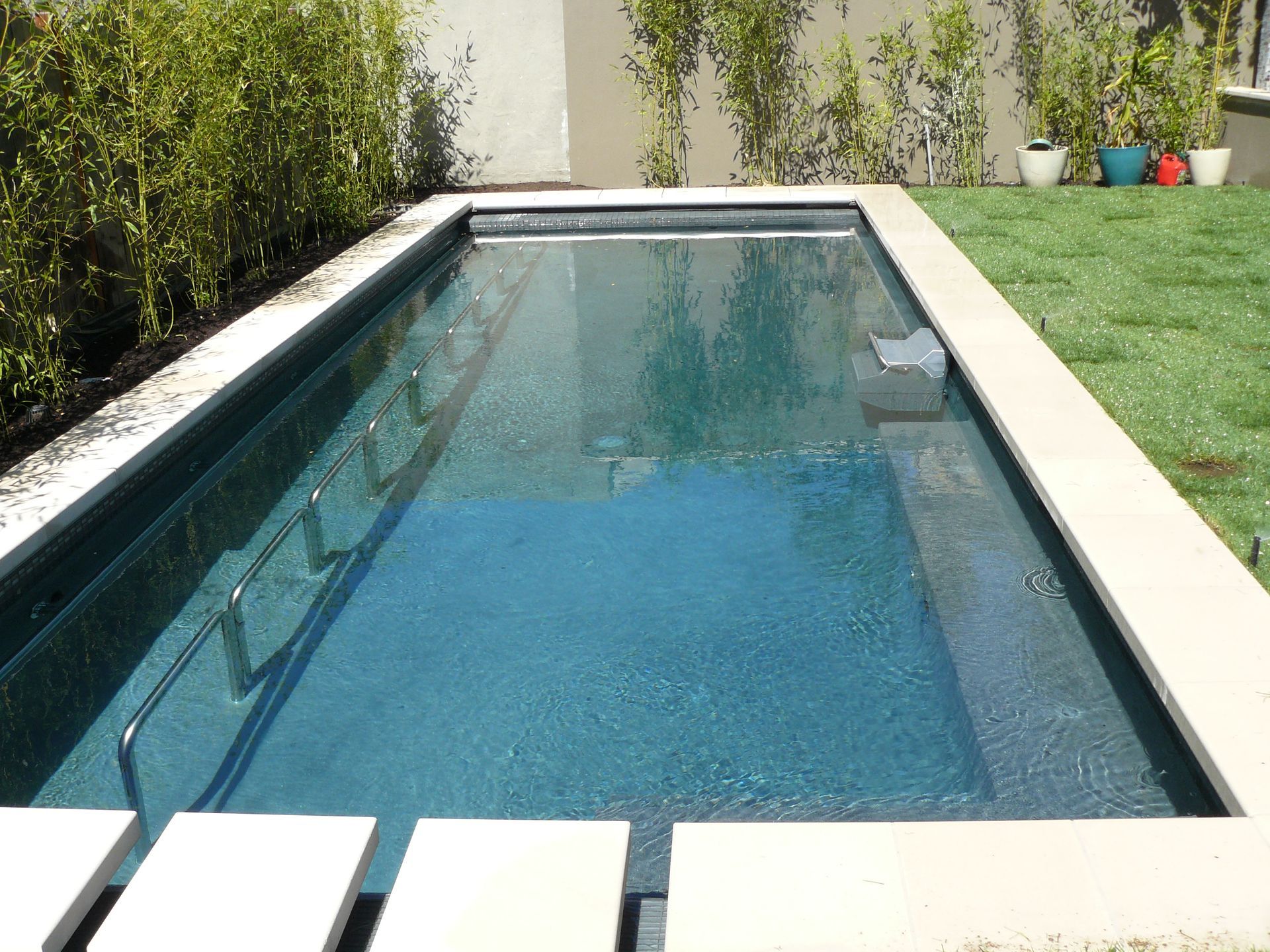 Long narrow backyard pool with clear blue water, white coping, and green lawn beside it