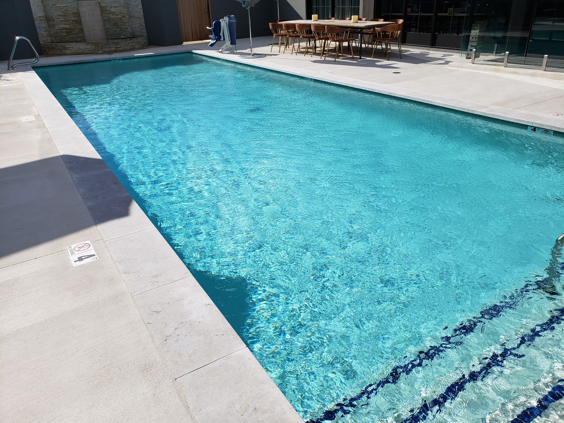 Outdoor swimming pool with clear blue water and surrounding concrete deck in bright sunlight