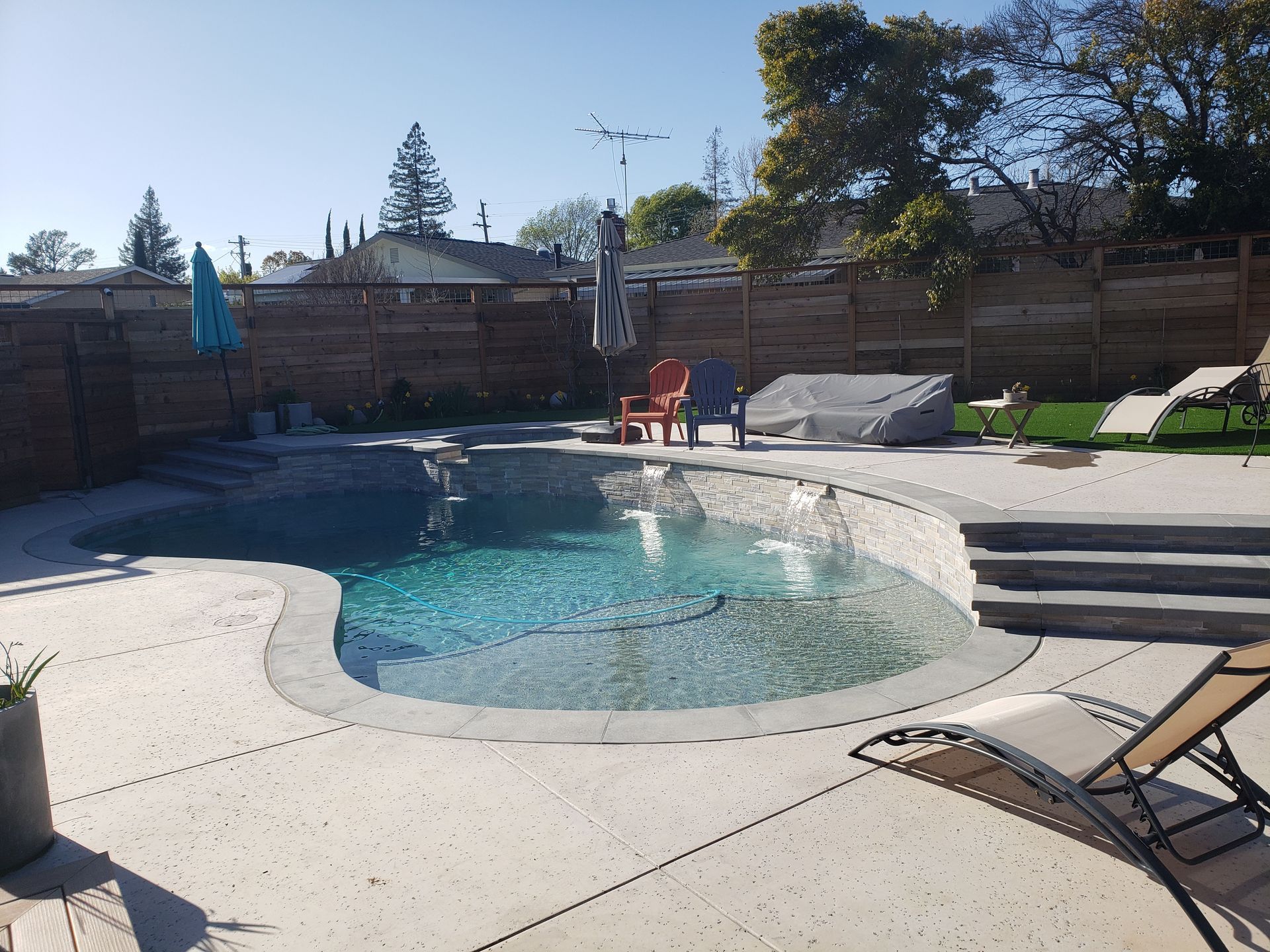 Backyard swimming pool with lounge chairs, brick wall, and two red chairs in the sun