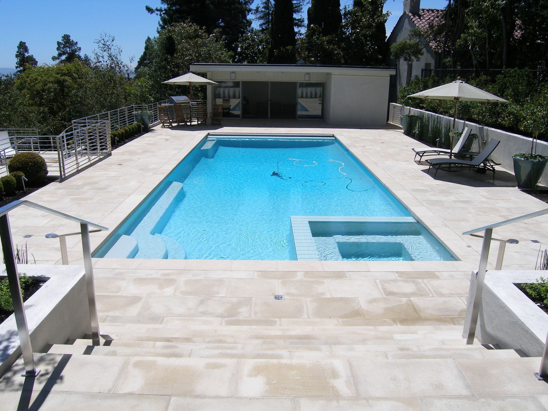 Backyard swimming pool with blue water, white patio, lounge chairs, and a small pool house in the background