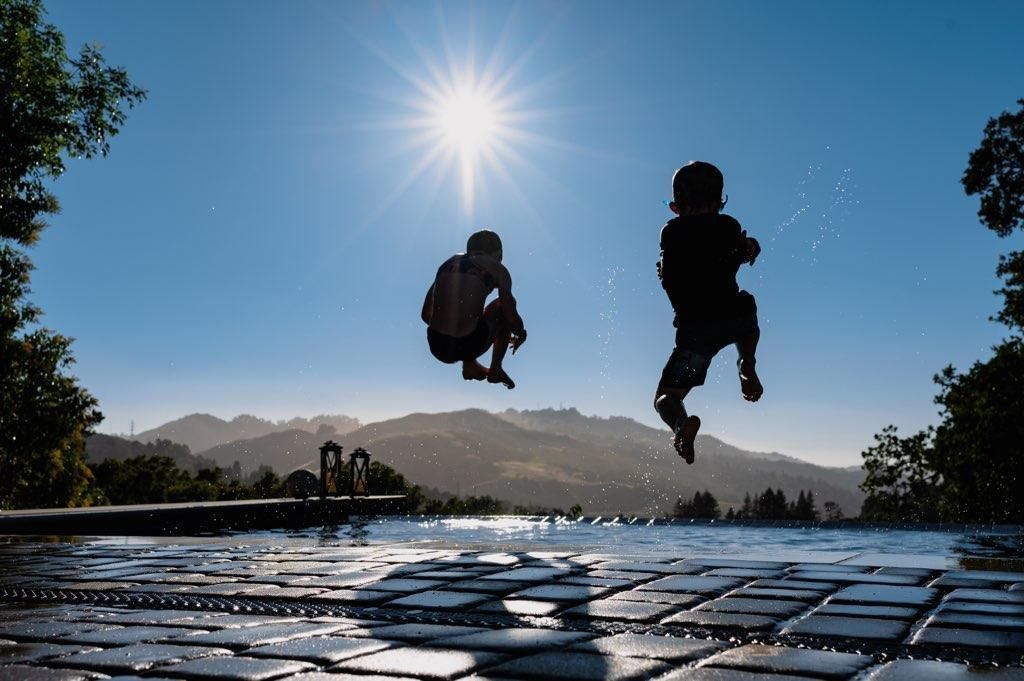 Two silhouetted hikers jump above a reflective stone path at sunrise with mountains in the distance