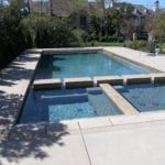Outdoor swimming pool with a shallow blue water section, concrete deck, and surrounding trees.