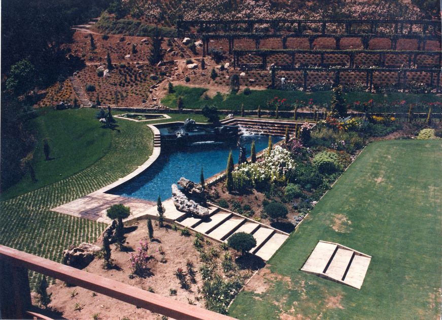 Man in white hat cleaning swimming pool with blue hose and vacuum.