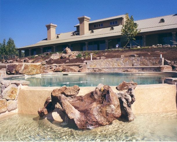 Pool with bright blue water, white buildings, and straw umbrellas under a sunny sky.