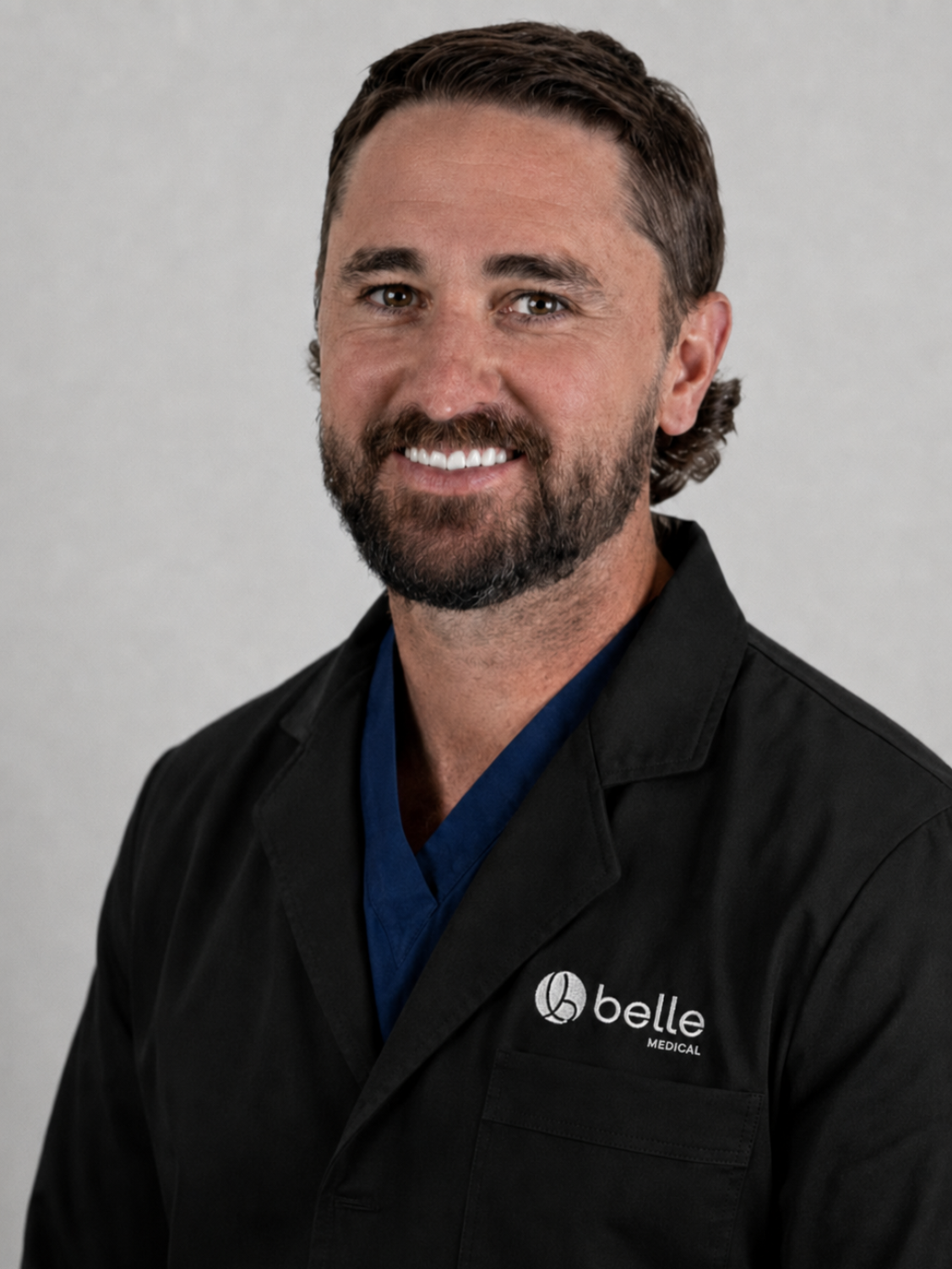Portrait of doctor Sean Reid, MD in a black jacket with a logo, against a light gray background