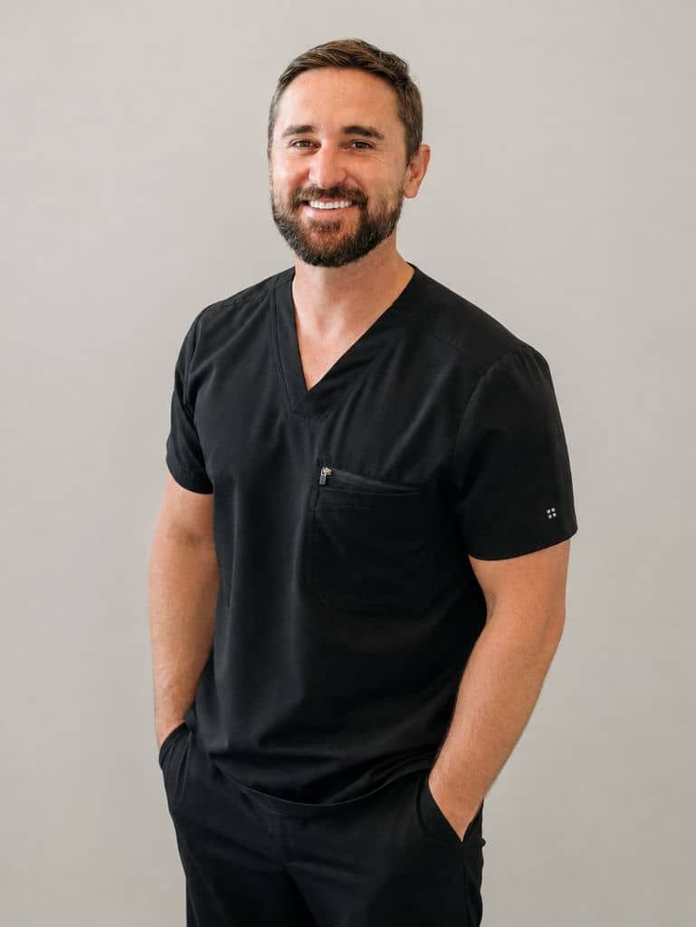 Doctor Reed in black scrubs standing against a light wall with hands in pockets