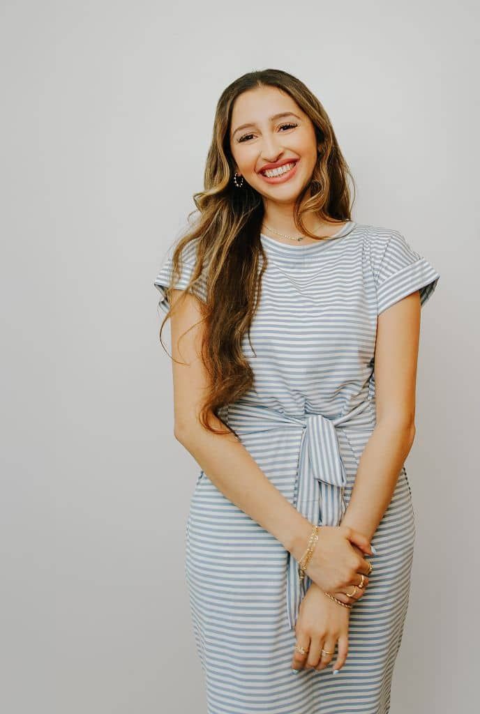 Woman in a striped dress smiling against a plain gray background