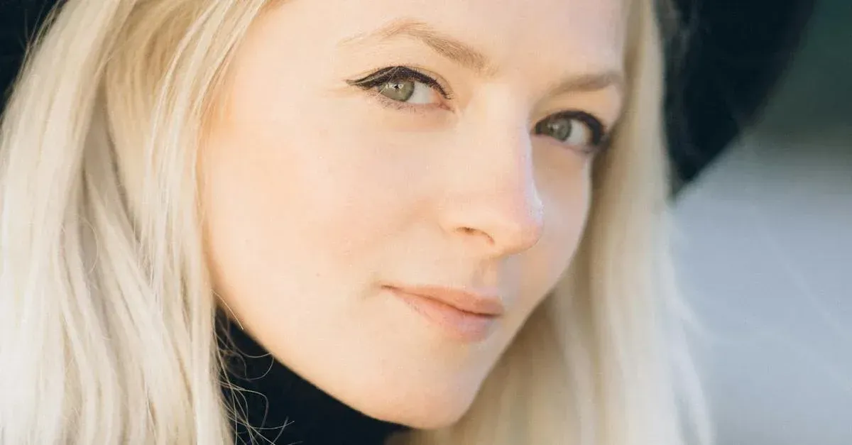 Close-up portrait of a blonde person smiling softly against a blurred dark background