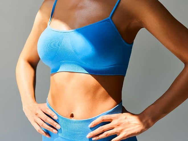 Woman in blue sports bra and shorts, standing with hands on hips against a gray background