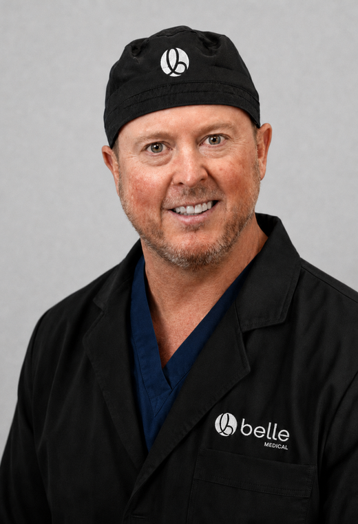 Doctor Patrick Blatchford in black work jacket and cap with logo, smiling against a light gray background.