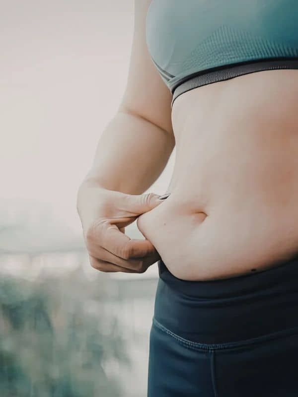 Person pinching belly fat in a sports bra and leggings outdoors