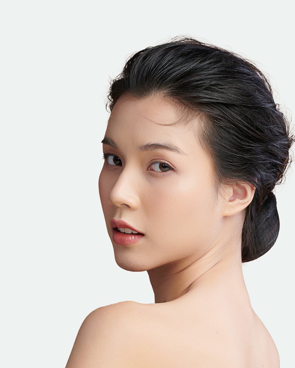 A woman with clear, even-toned skin looking over her bare shoulder