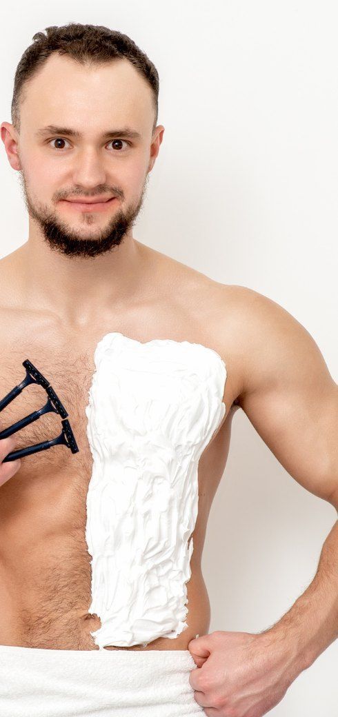 A man with shaving cream on half of his chest, holding three razors