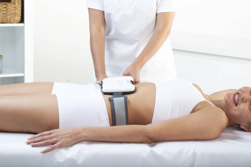 Woman lying on a treatment table during a body muscle stimulation procedure with a handheld device.