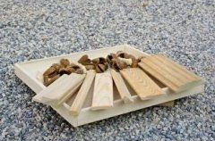 Trappole per topi in legno disposte in fila, con esca di arachidi su una superficie ghiaiosa.