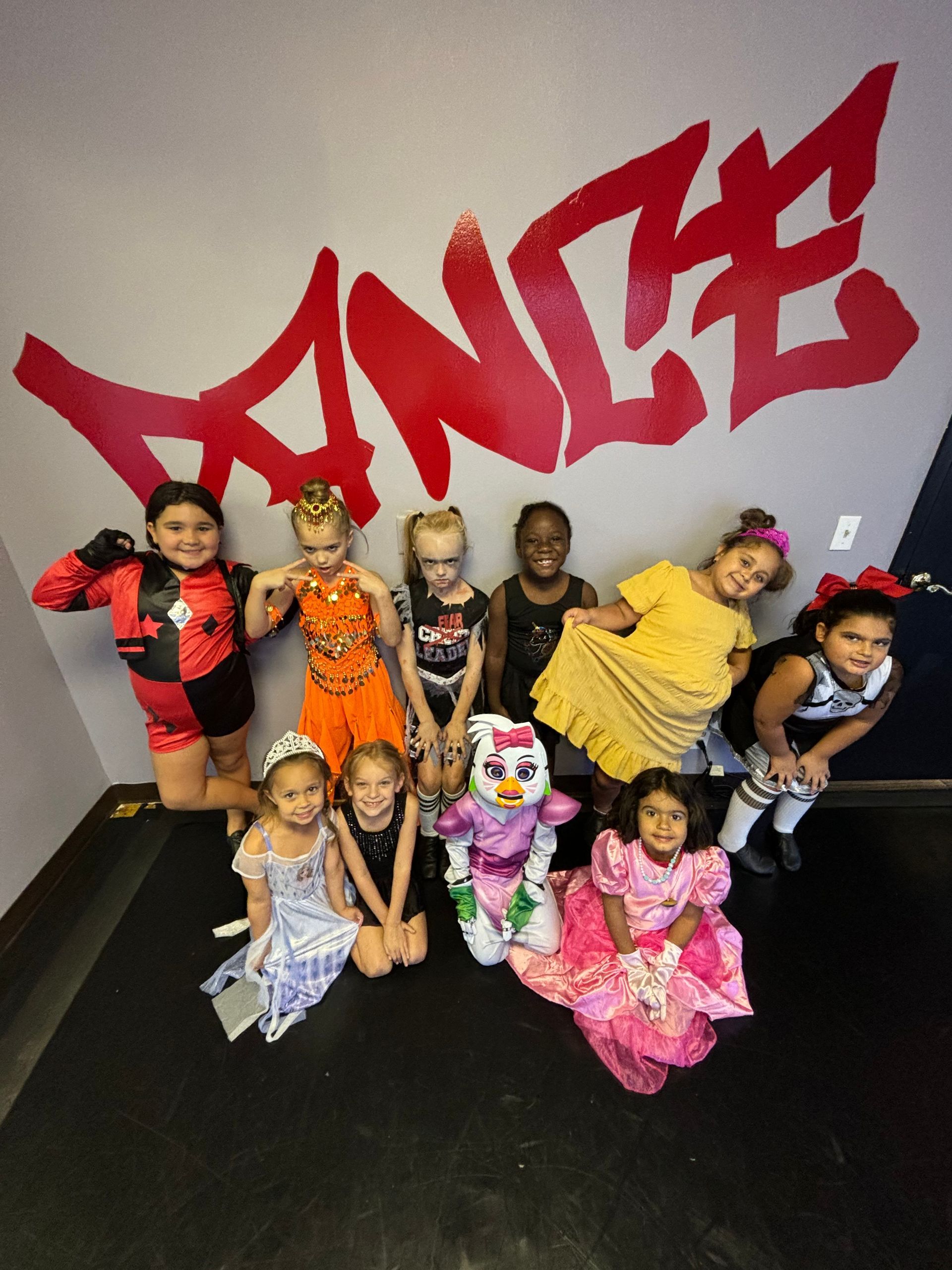 A group of children posing for a picture in front of a wall that says dance