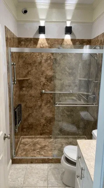 A modern bathroom features a glass-enclosed shower with brown marbled walls, a wall-mounted seat, and overhead spotlights.