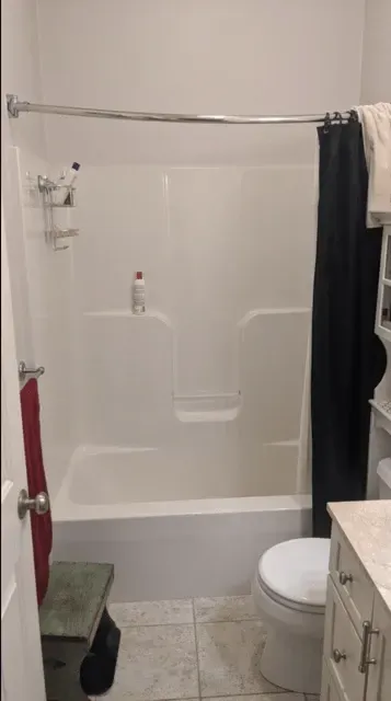 A small, tiled bathroom featuring a white bathtub with a curved shower rod and black curtain, a toilet, and a vanity.